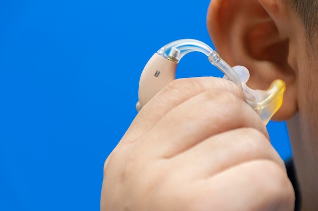 Hand that is catching hearing aid To wear It is his first device Blue background To live in society