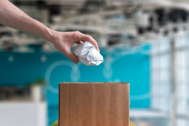 A hand throw the crumpled paper piece in the trash basket