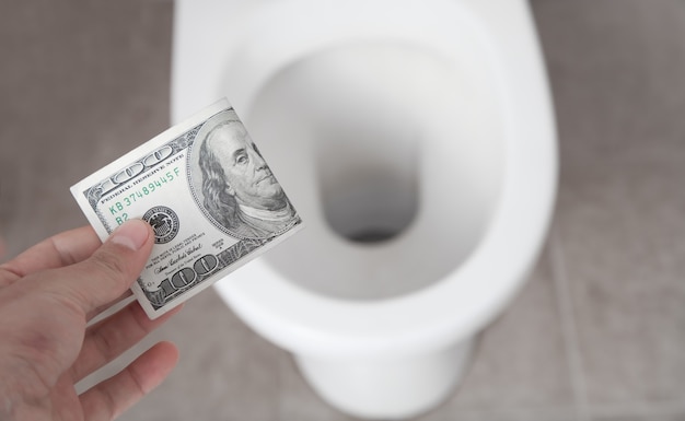 Hand throwing hundred dollar down the toilet.