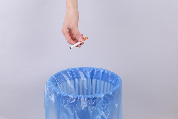 Рука бросает сигарету в мусорное ведро с пакетом на сером фоне