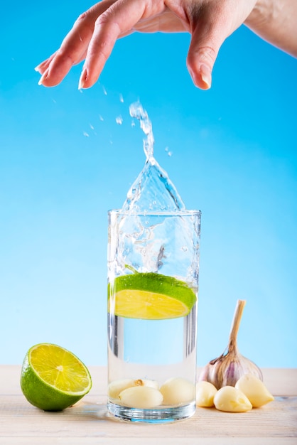 Hand throws lime into a glass of water with garlic on blue 