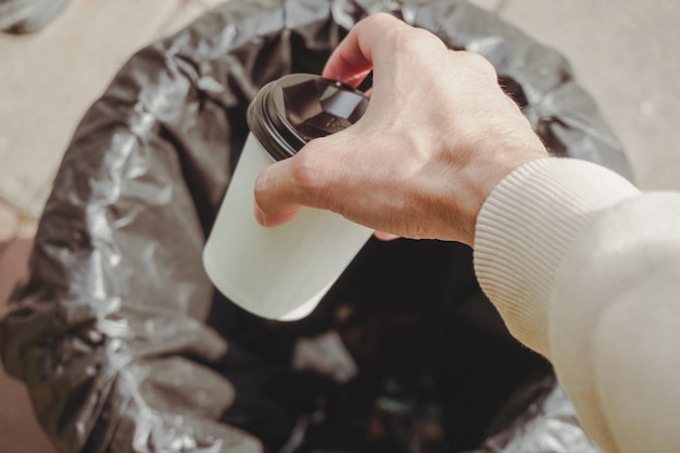 A hand throws a paper cup into the trash can