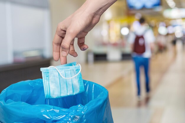 Hand throws a protective mask into the trash can on a blurred background