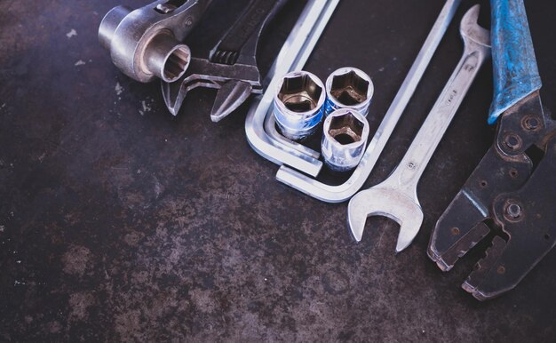 Ручные инструменты, состоящие из гаечных ключей, плоскогубцев, торцевых ключей, выложенных на фоне старой стальной пластины