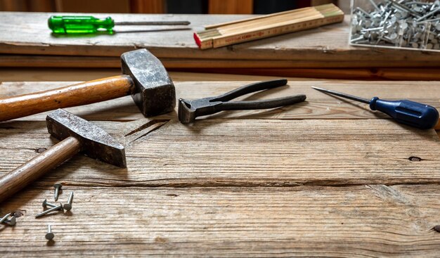 Hand tools old used hammer sledgehammer plincers and nail on\
wood work bench table