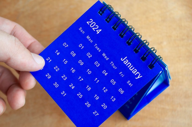 Hand toont kalender van januari 2024 op houten achtergrond Kalender en nieuwmaandconcept