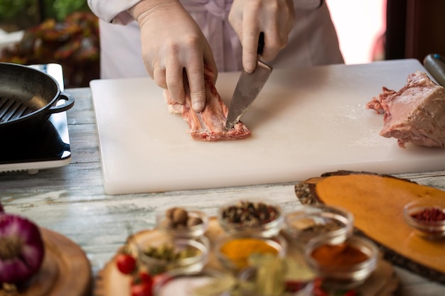 Hand touches meat with knife. White cooking board and pan. Clean off pork fat. Chef is busy at work.