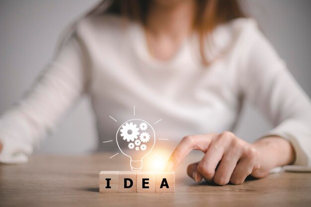 Mano che tocca la lampadina sul blocco di legno con word idea, nuovo concetto di idea con innovazione e ispirazione, tecnologia innovativa nel concetto di scienza e comunicazione.