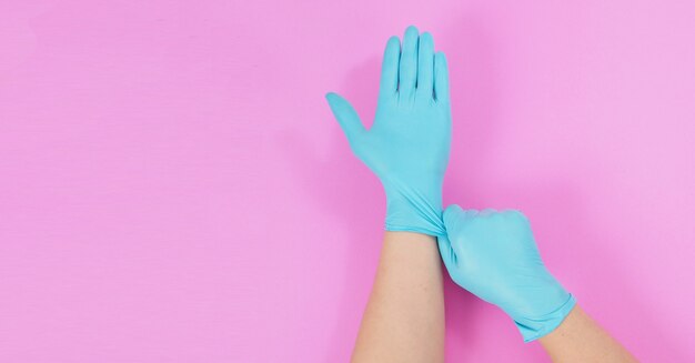 Hand trekt blauwe latexhandschoenen op roze achtergrond.