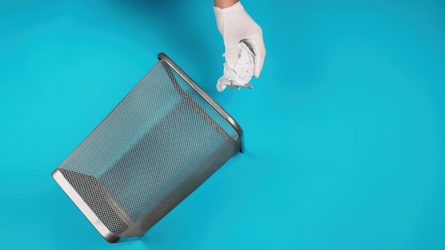 Hand trowing a paper into a wastebasket on blue background