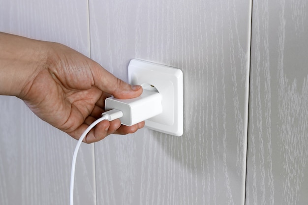 Hand turns on, turns off charger in electrical outlet on wall