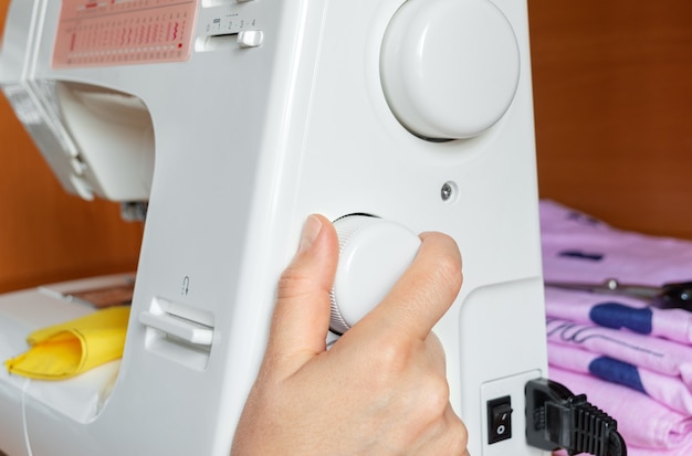 The hand turns the wheel of the sewing machine to adjust the stitch type, close-up.