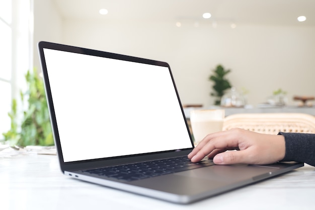 a hand typing and touching laptop with blank white desktop screen on table in cafe