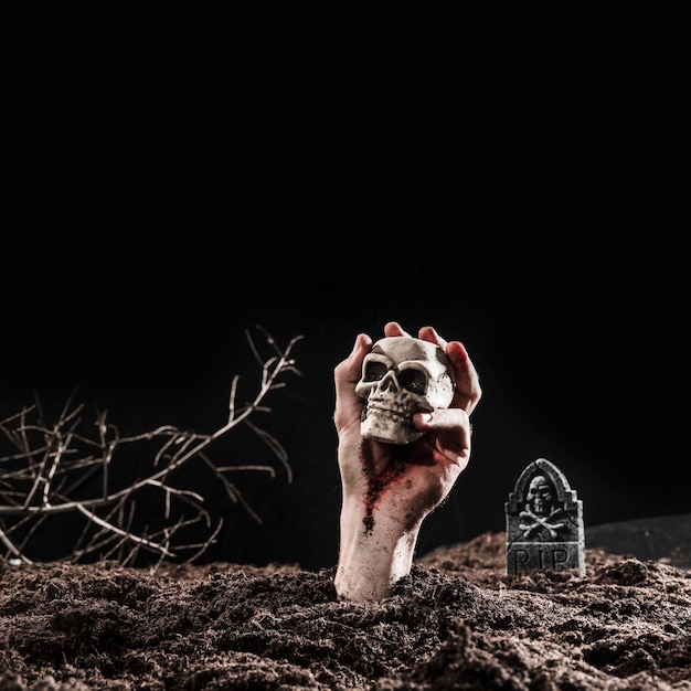 Photo hand of undead holding skull at dark graveyard on halloween night