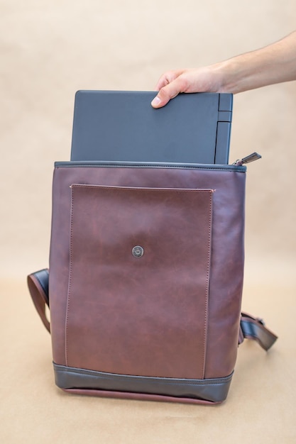 Hand of unrecognizable person putting laptop in leather\
bag