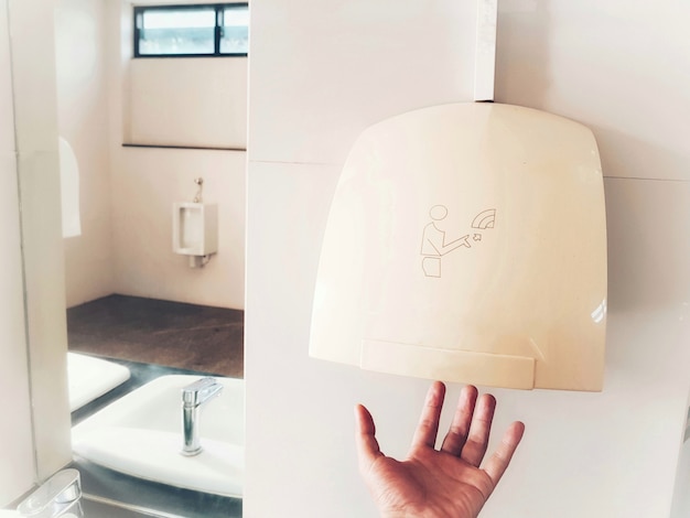 Hand using automatic hand dryer after toilet for hygiene.