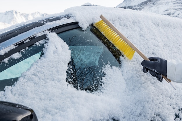 Mano usando spazzaneve spazzare la neve sul parabrezza dell'auto