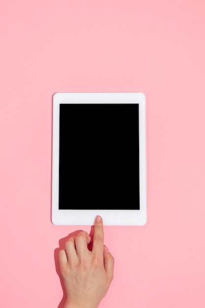 Hand using gadgets, tablet on top view, blank screen with copyspace, minimalistic style. Technologies, modern, marketing. Negative space for advertising. Coral color on background. Stylish, trendy.