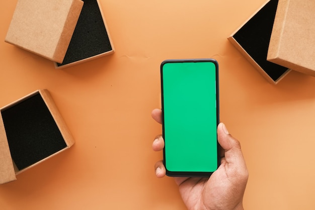 Фото Рука с помощью смартфона с зеленым экраном и пустой подарочной коробкой на столе