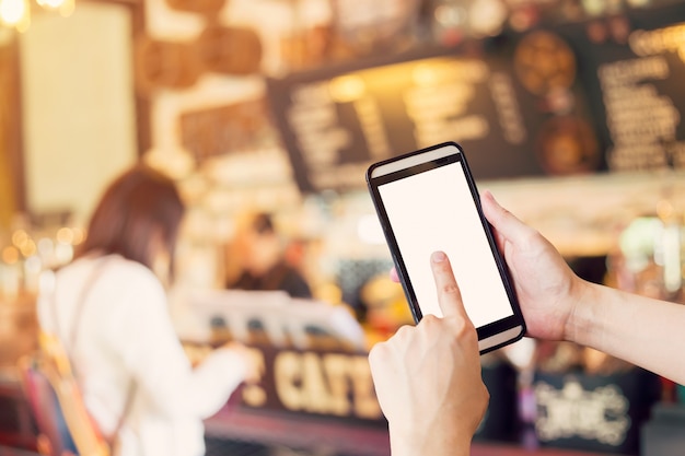 Mano utilizzando smartphone e persone sfuocate in caffè con tono d'epoca.