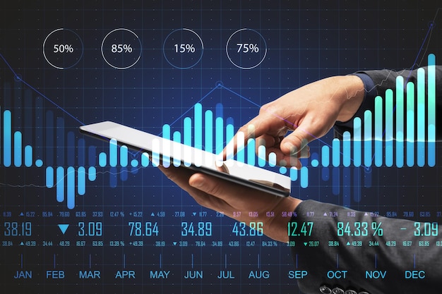 Hand using tablet on desktop with abstract forex chart hologram