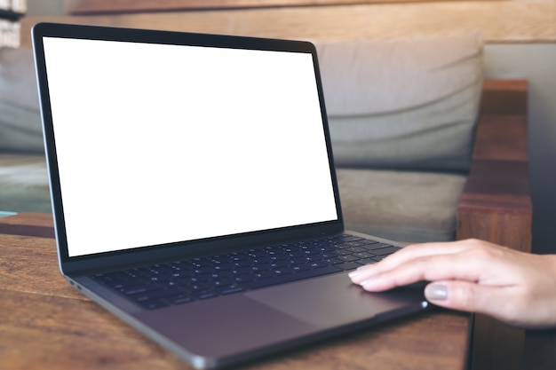 a hand using and touching laptop with blank white desktop screen on wooden table in cafe