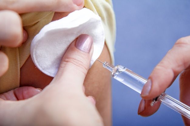 Hand van arts die spuit voor vaccinatie vasthoudt aan de bovenarm van de patiënt voor preventie van griepziekte. Selectieve focus op spuit