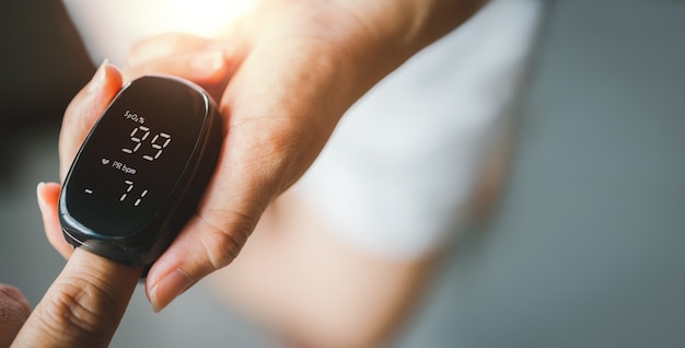 Hand van aziatische vrouw met een aangesloten pulsoximeter op vingertop, controle van het zuurstofverzadigingsniveau in het bloed, diagnose van Coronavirus of COVID-19 thuis, gezondheidszorg