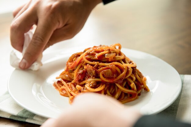 Hand van chef-kok afvegende schotel van spaghetti bolognese