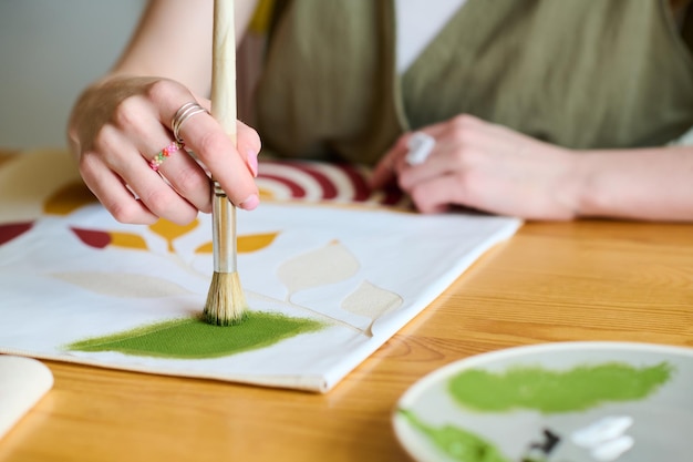 Hand van creatieve vrouwelijke artiest die met penseel groene waterverf op papier zet