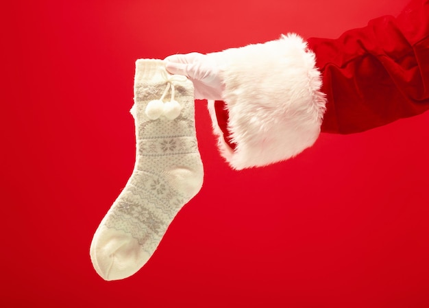 Hand van de kerstman met een kerst gebreide sokken op rood