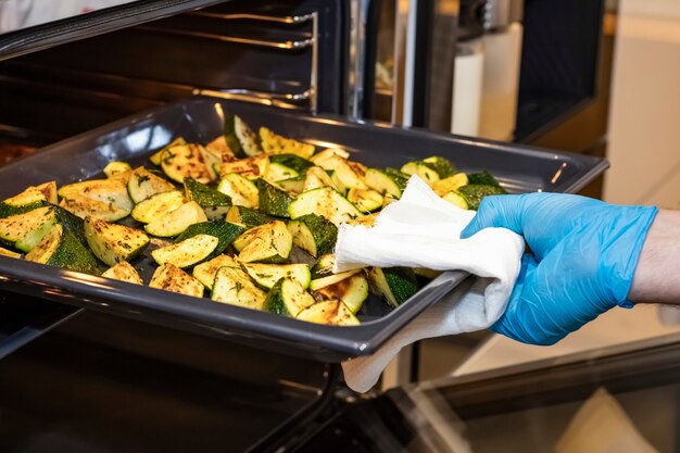 Hand van de kok haalt uit de oven een vel van het dienblad met gebakken courgette