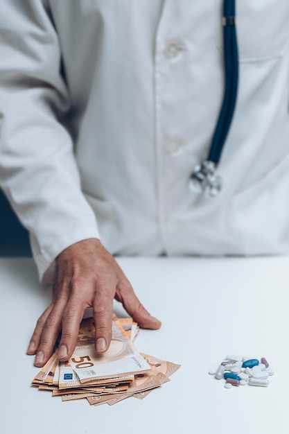 Hand van dokter die een hoop rekeningen neemt naast een hoop pillen op witte tafel