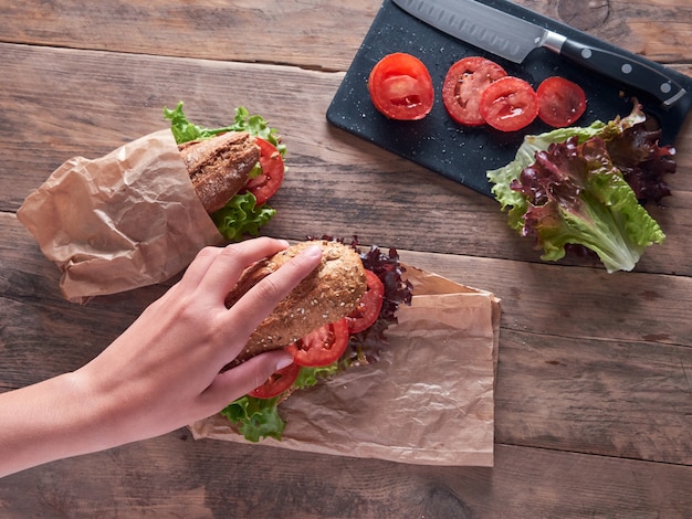 Hand van een jong meisje dat een stokbrood met sla en tomaat bereidt