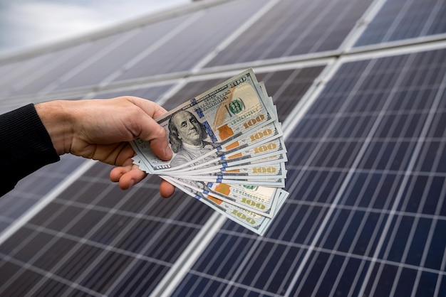 Hand van een jonge man die dollars vasthoudt voor de installatie van nieuwe zonnepanelen Groen elektriciteitsconcept