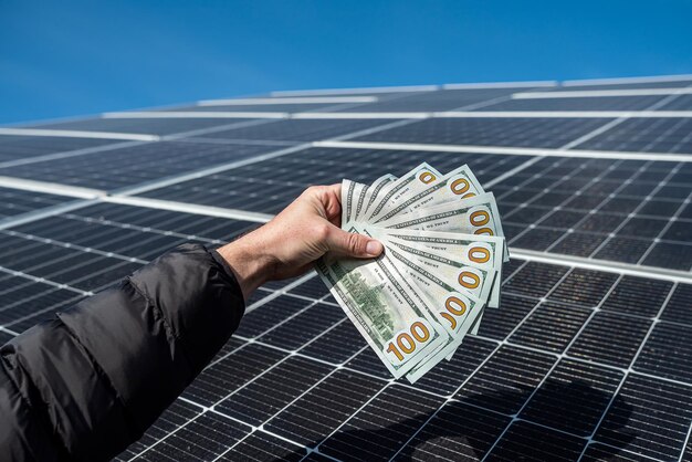 hand van een jonge man met dollars op geïnstalleerde nieuwe zonnepanelen Concept van groene elektriciteitsbesparing