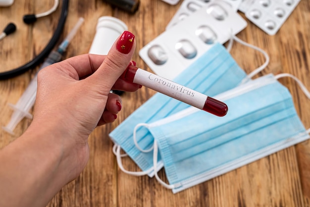 hand van een jonge vrouw die een reageerbuis met bloed vasthoudt op een achtergrond van medicijnen en maskers. geneeskunde concept