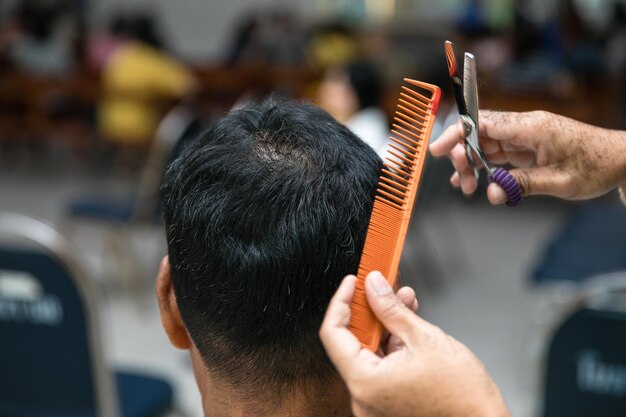 Hand van een kapper die het haar van een man knipt met schaar en kam in een kapperswinkel