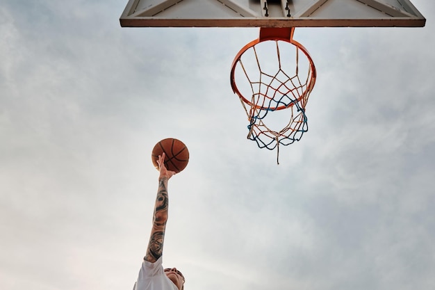 Hand van een man die basketbal gooit naar de baskethoop baskethoop en bal tegen bewolkte lucht.