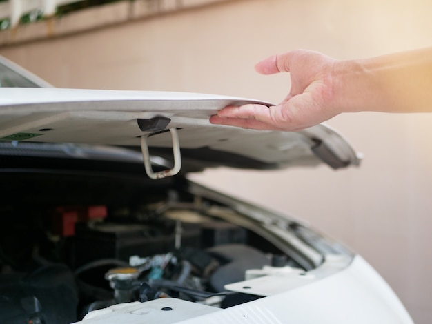 Foto hand van een man die de motorkap opent om de algemene staat van de auto, motor, olie, radiator te controleren.