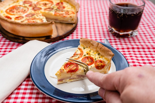 Hand van een man die het gedeelte van ham en kaascake of Quiche Loraine snijdt die op een plaat wordt gediend. Thuis eten, gezond concept