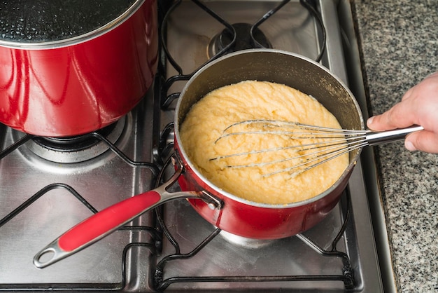 Hand van een persoon die maïszetmeel kookt in een pot op een keukenfornuis