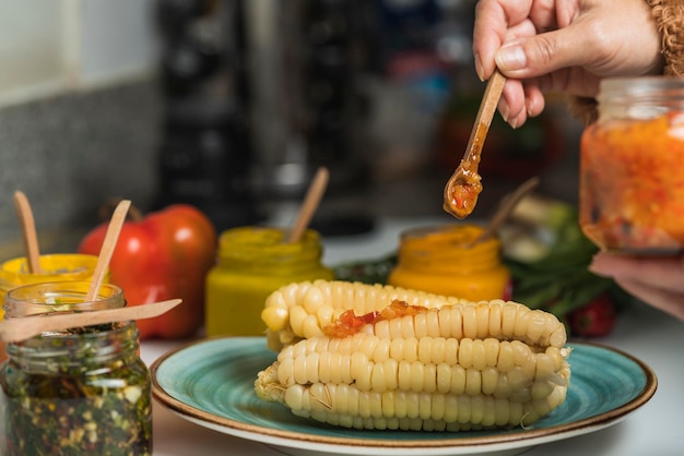 Hand van een persoon die saus op een schotel met mais met Rocoto-saus smeert