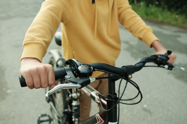 Hand van hedendaagse tiener die fiets duwt terwijl hij over de weg in het park rijdt terwijl hij op zijn gemak geniet van de promenade promenade