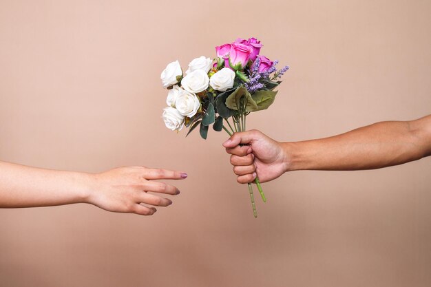 Hand van jonge man geeft boeket bloemen aan vrouw geïsoleerd op beige studio achtergrond