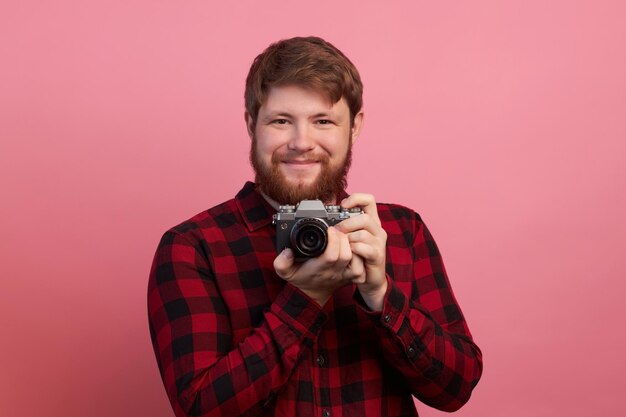 Hand van jonge Spaanse man met vintage camera over geïsoleerde roze achtergrond