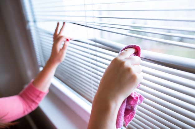 Hand van jonge vrouw die jaloezieën schoonmaken door roze doek huishoudelijk werk, schoonmaakster