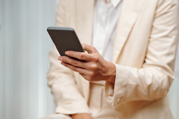 Hand van jonge vrouw in beige blazer sms'en in mobiele telefoon