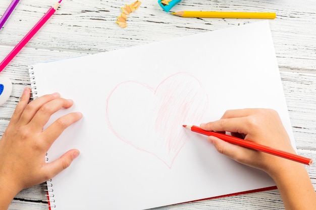 Hand van kinderen tekenen rood hart met kleurpotlood op wit papier op houten tafel.