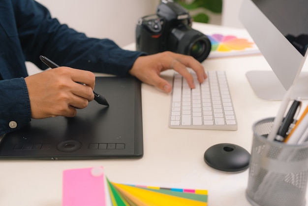 Hand van mannelijke ontwerper die aan zijn bureau werkt met stylus en digitale grafische tablet.